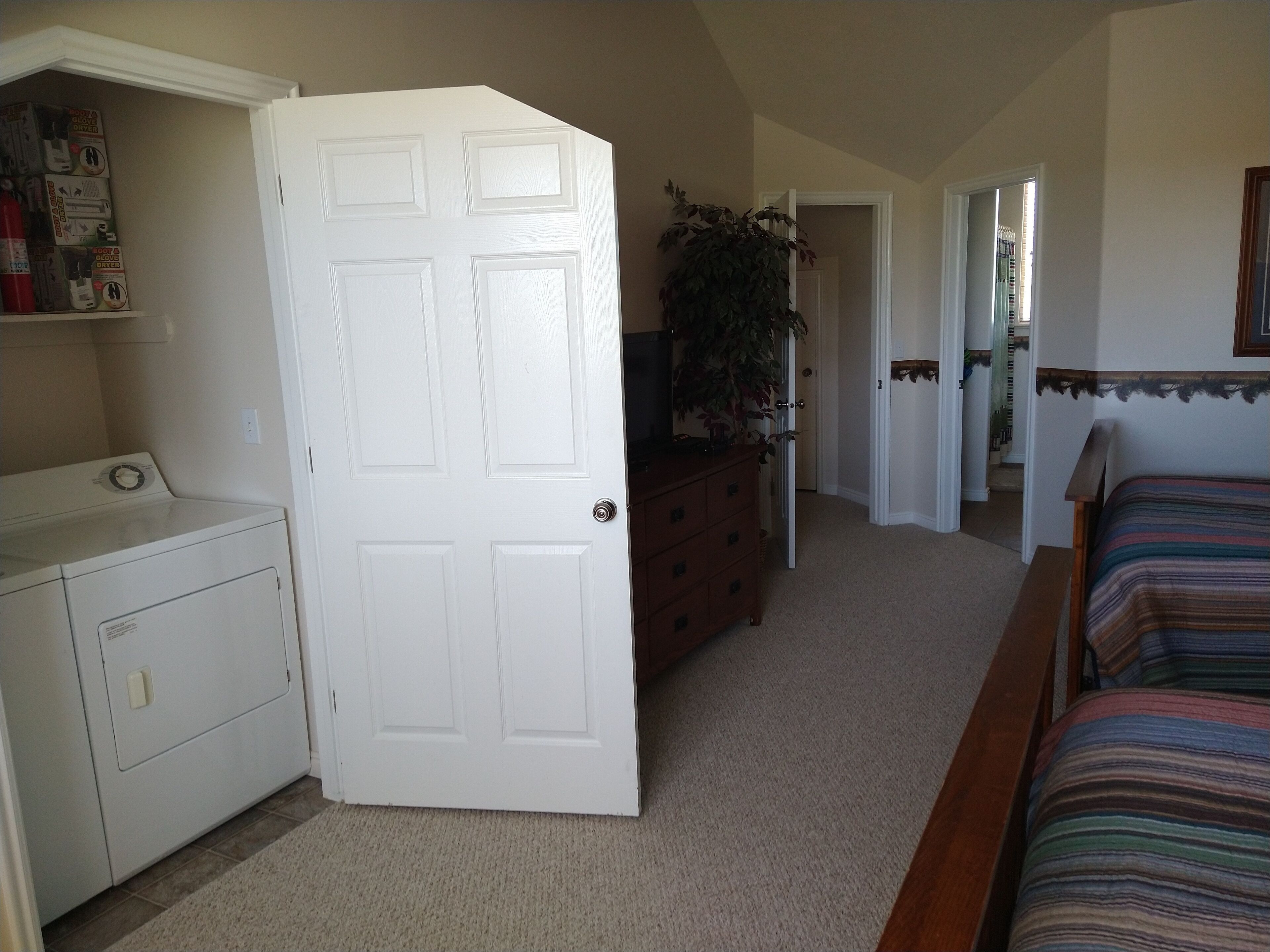 A bedroom with a bed, a dresser, a washing machine, and a door leading to another room.