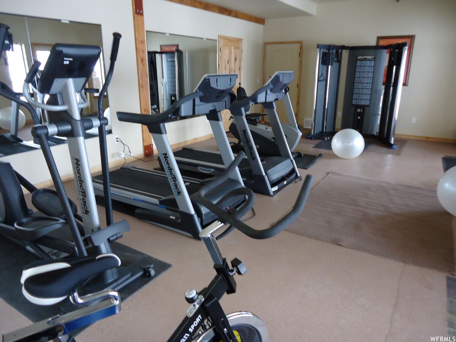 Uma academia com esteiras e bicicletas ergométricas, um espelho e uma porta que dá para outro espaço.