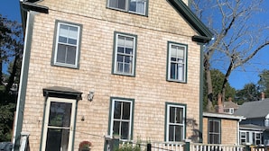 A two-story building with a brick facade, multiple windows, a front porch with a railing, and a stone pathway leading to the entrance.