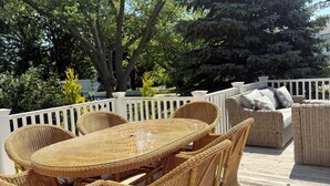 A wicker outdoor dining set with a glass table and chairs, surrounded by a wooden deck and white railings.