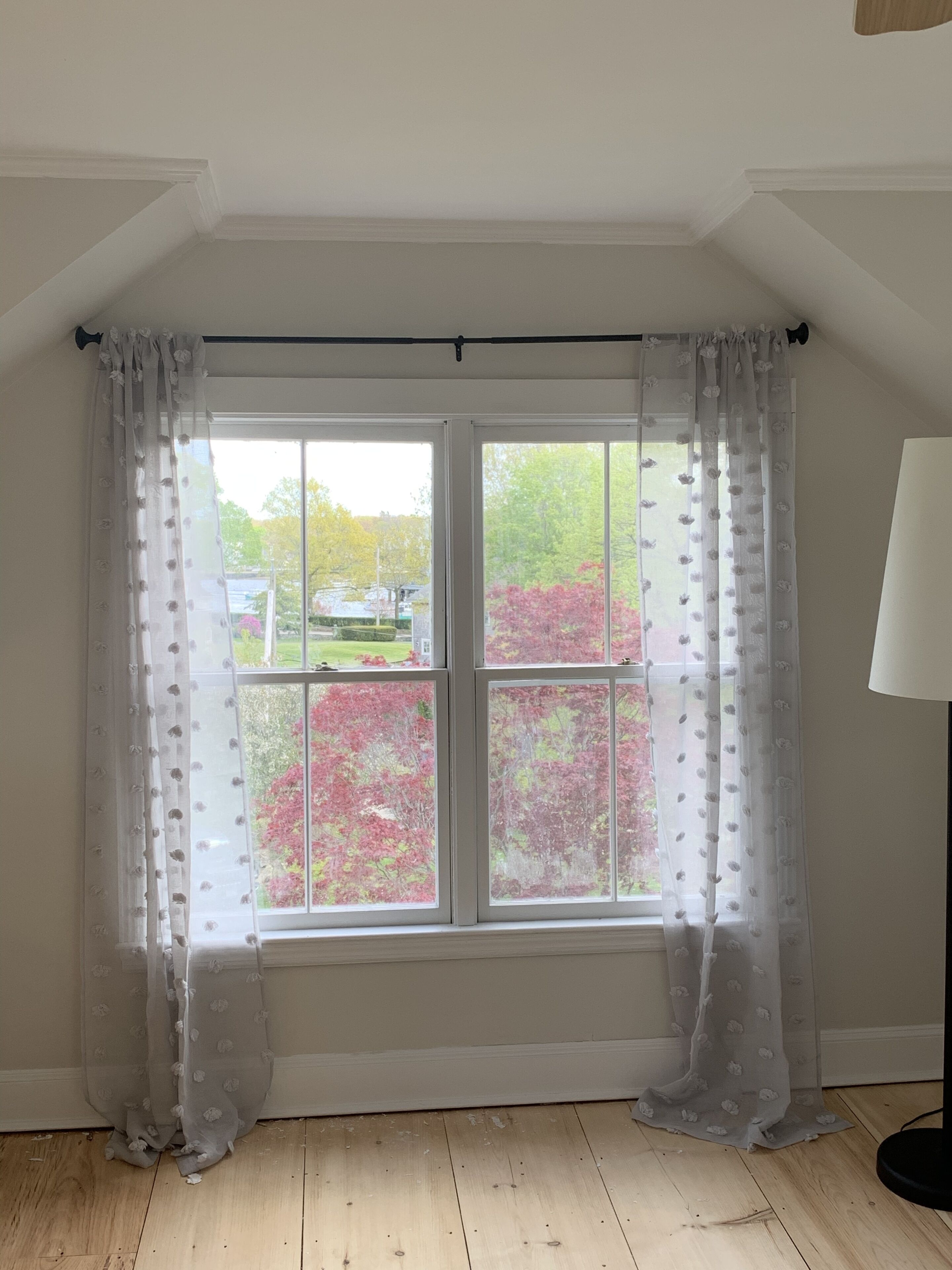 A room with a large window, white curtains, and a wooden floor.