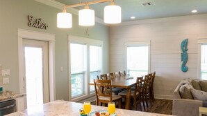 A kitchen with a marble countertop, wooden chairs, and a dining table. There are two glasses of orange juice and a plate with cookies. - Gorgeous Beach View - 2nd Street back  - 4/3 2 Story (Galveston)