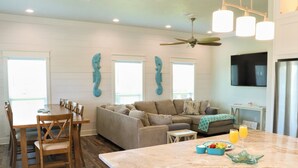 A spacious living area with a wooden dining table and chairs, a sofa, and a kitchen area with a marble countertop. - Gorgeous Beach View - 2nd Street back  - 4/3 2 Story (Galveston)