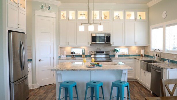 A modern kitchen with white cabinets, a stainless steel refrigerator, a microwave, and a large island with bar stools. - Gorgeous Beach View - 2nd Street back  - 4/3 2 Story (Galveston)