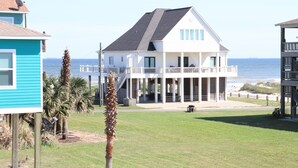 A two-story house with a balcony overlooking the beach, a grassy yard, and a view of the ocean. - Gorgeous Beach View - 2nd Street back  - 4/3 2 Story (Galveston)