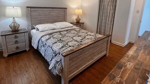 A bedroom with a wooden bed, two bedside tables, a nightstand, a patterned bedspread, and a wooden dresser.