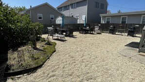 A residential backyard with a gravel patio, a wooden fence, and a large house with a sloped roof.