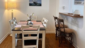 A dining area with a wooden table and chairs, a lamp, a painting of a ship, a clock, and a shelf with a lamp.