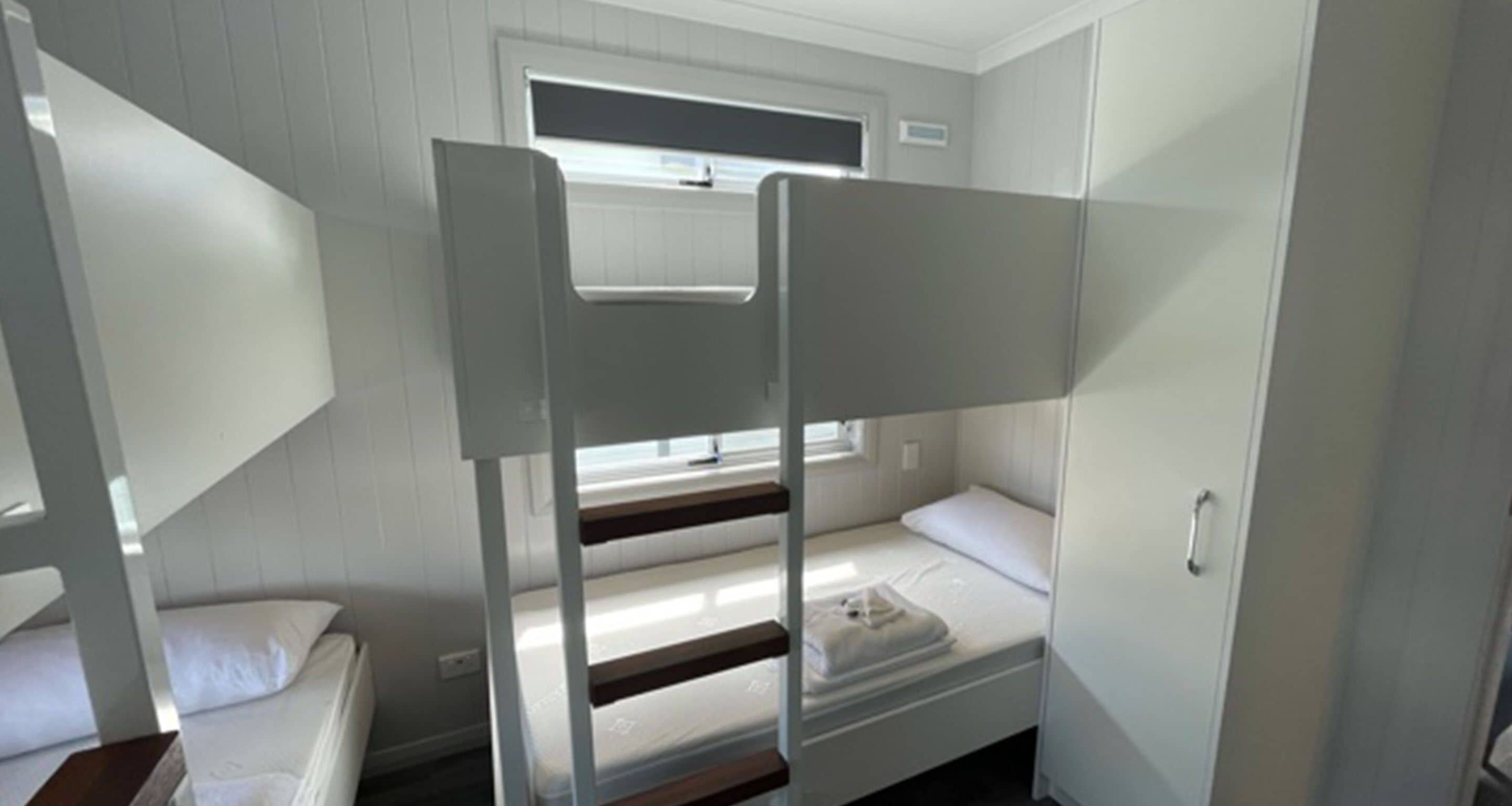 Une chambre avec un lit superposé, une fenêtre, une porte et une petite table.