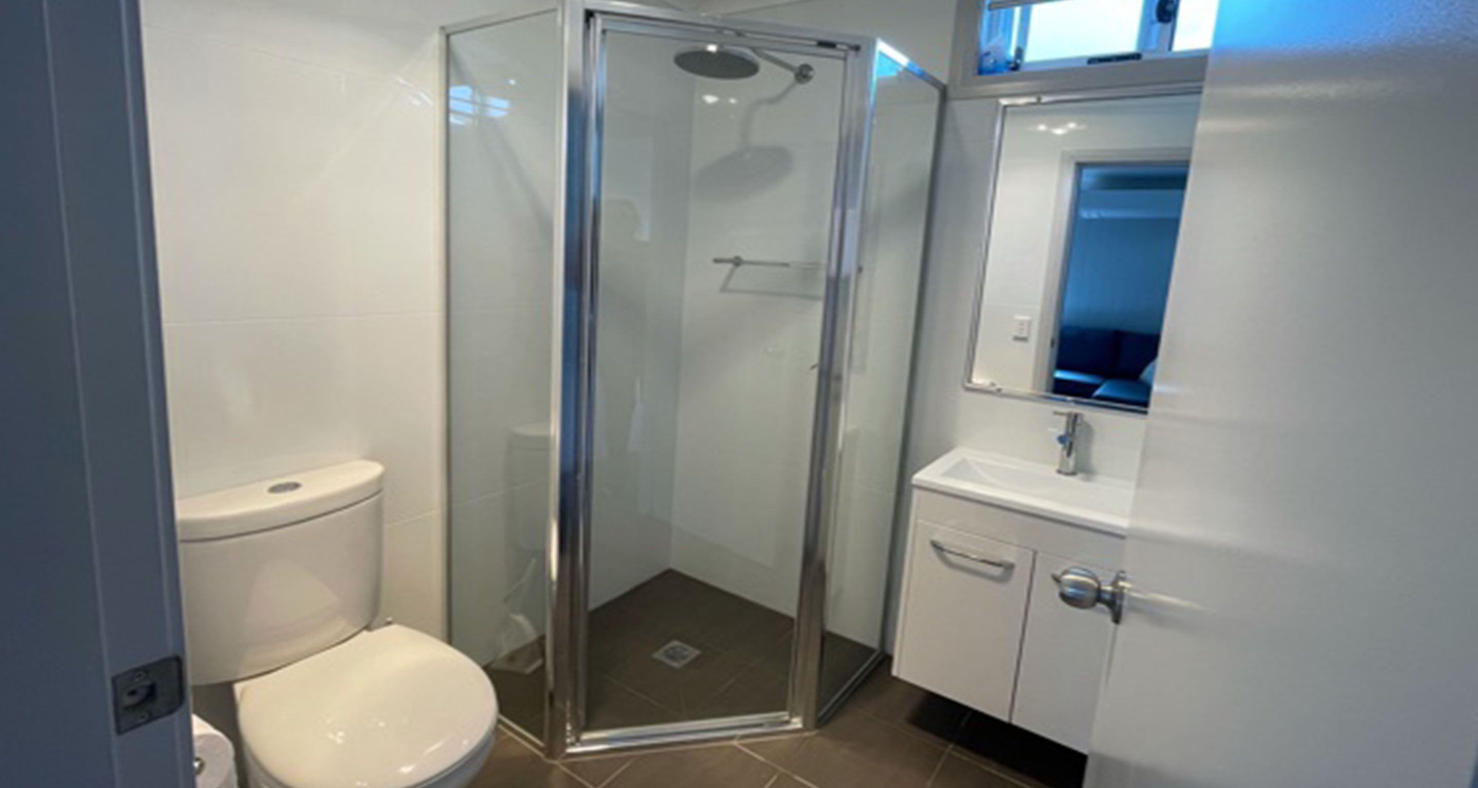 A bathroom with a glass-enclosed shower, a white toilet, and a sink with a mirror above it.