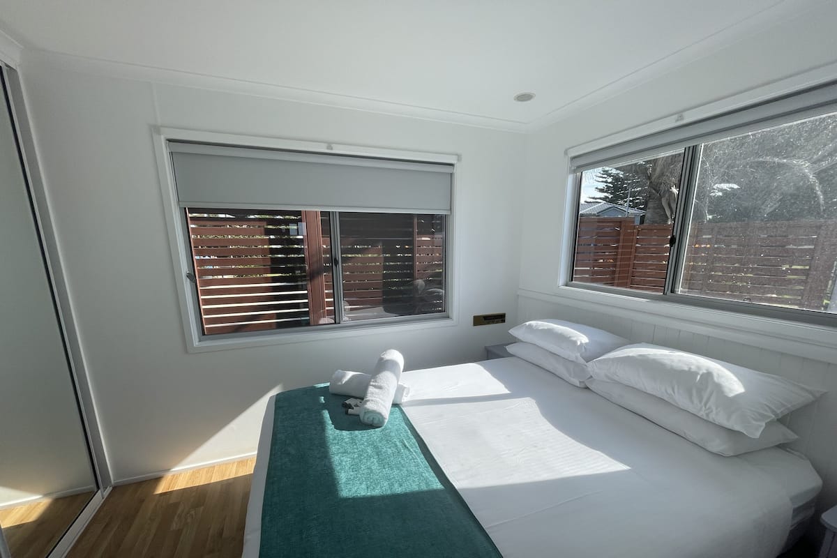 Une chambre à coucher avec un lit, une fenêtre avec des stores et une vue sur un mur de briques à l’extérieur.
