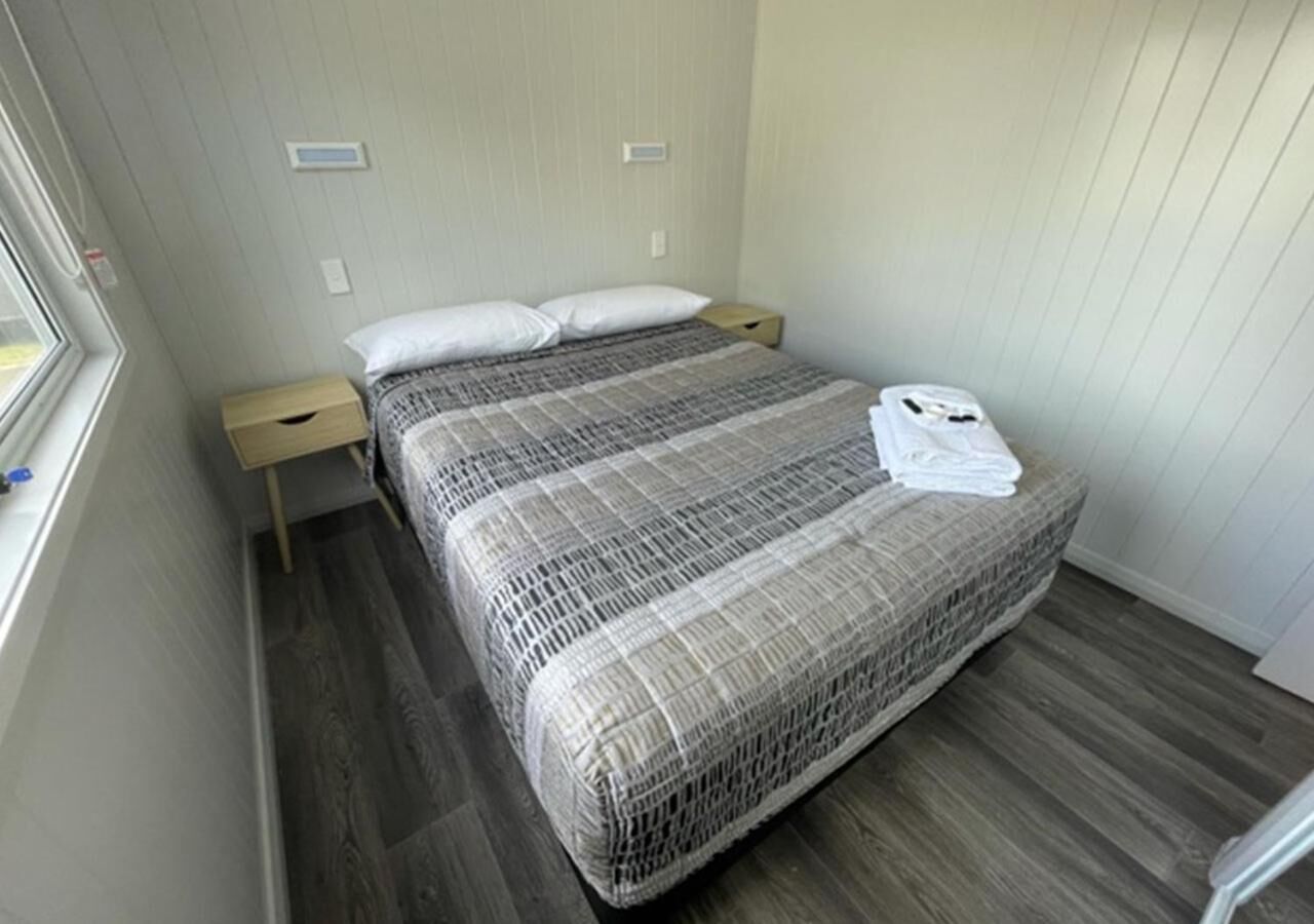 A neatly made bed with a patterned bedspread, a bedside table, and a window on the left side.