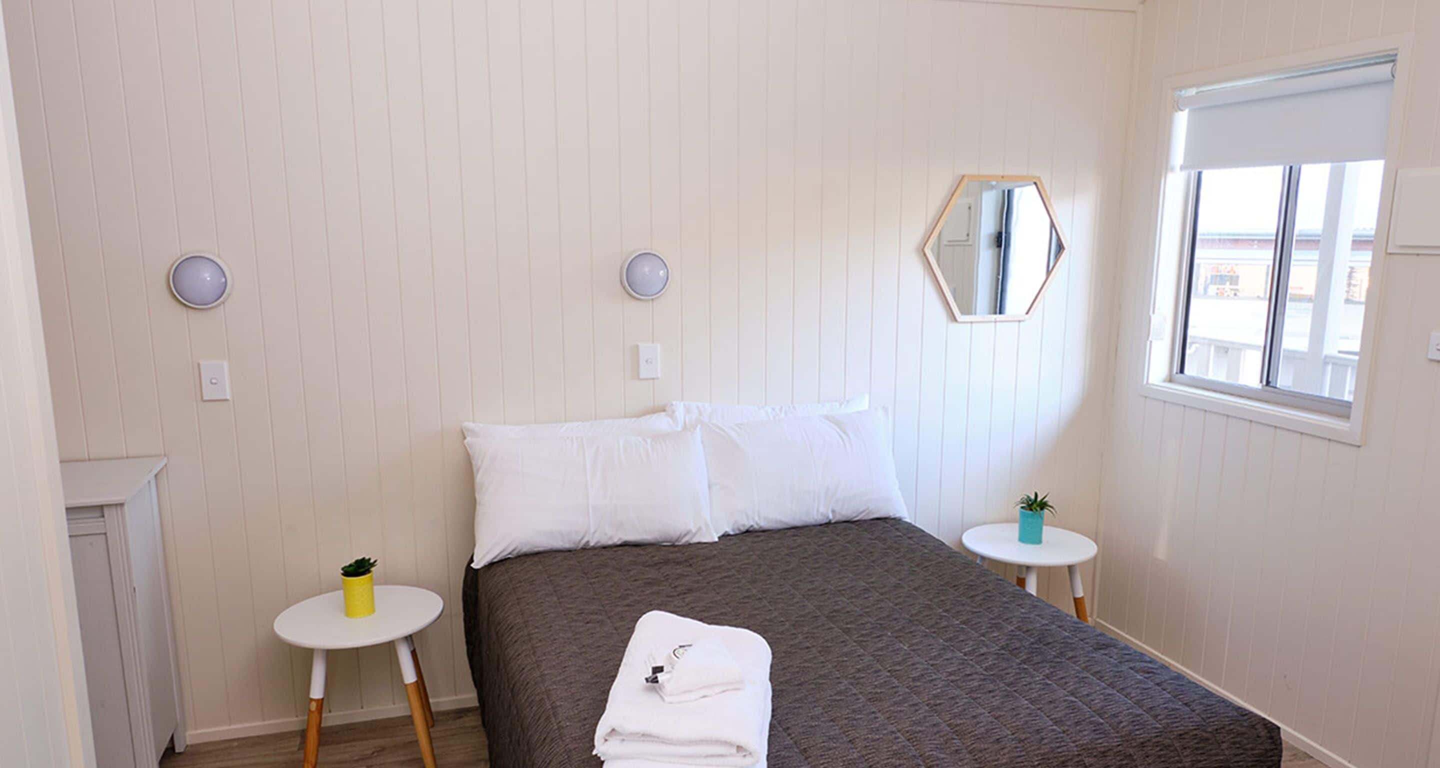 A bedroom with a bed, two bedside tables, a mirror, and a window.