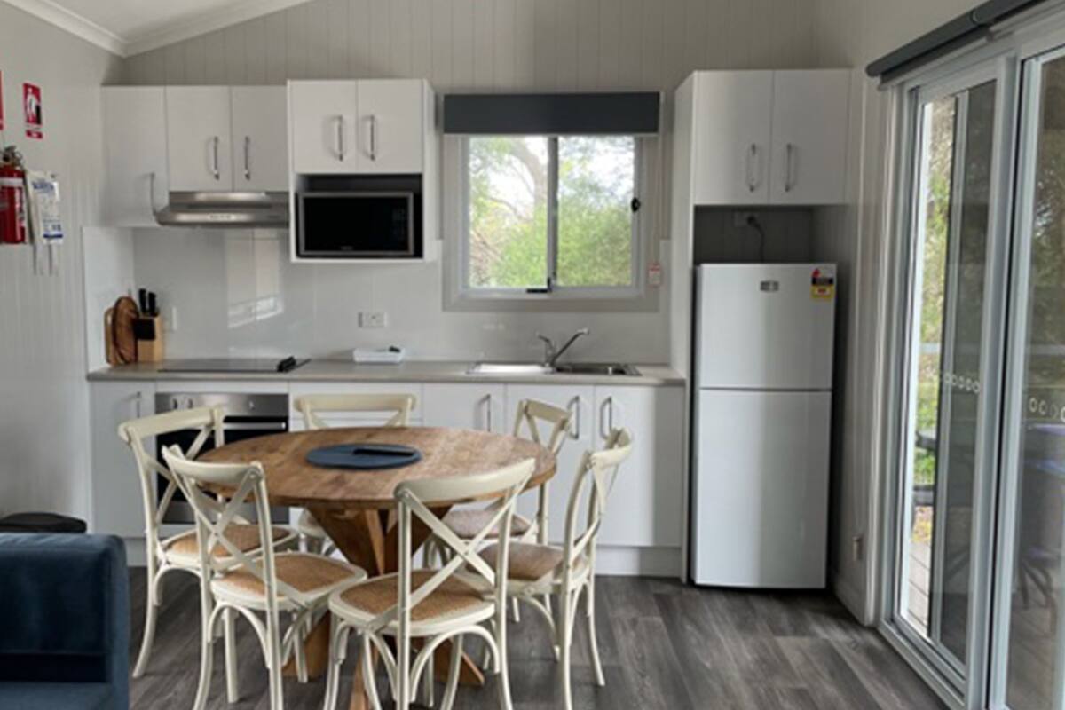 Une cuisine moderne avec des meubles blancs, un îlot central doté de chaises, un four à micro-ondes encastré et un réfrigérateur.