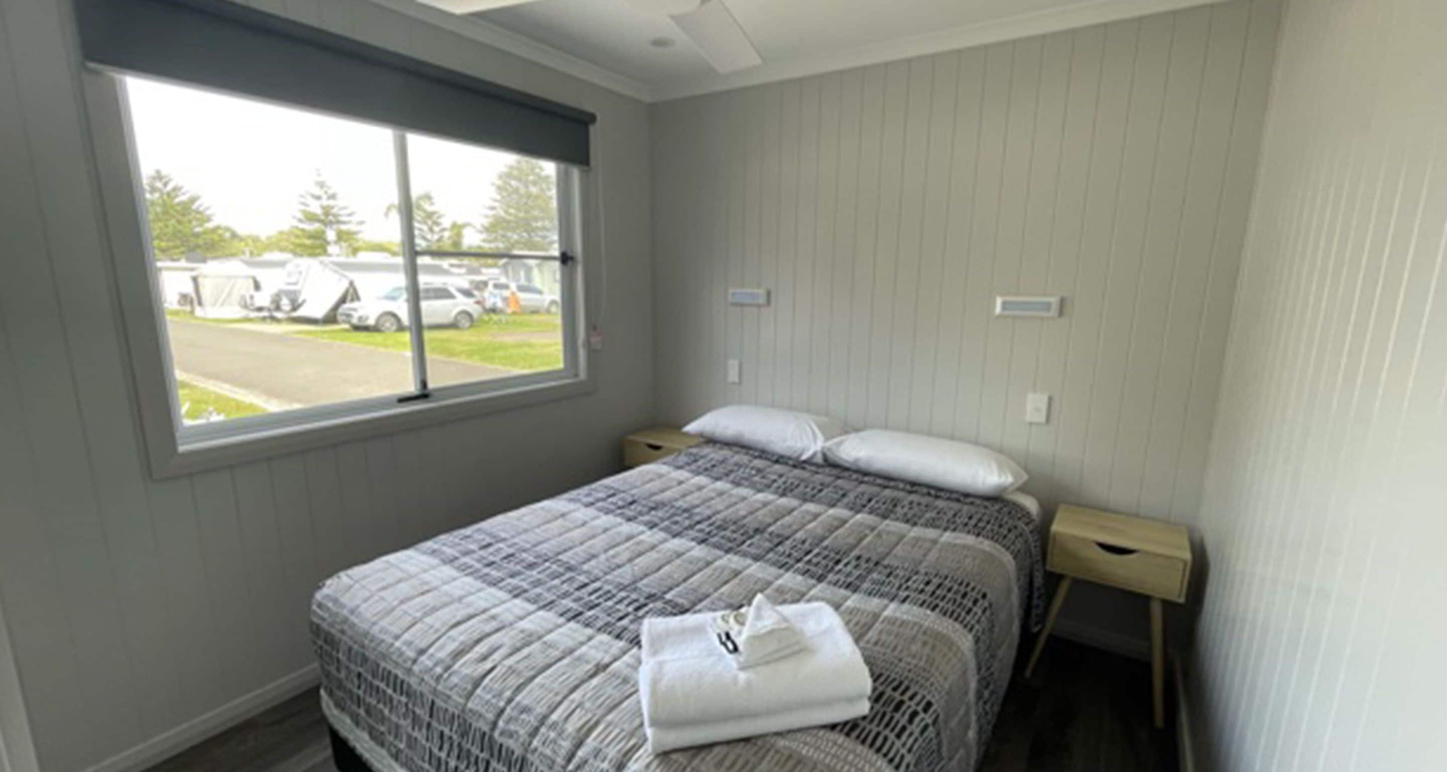 Un dormitorio con una cama, un ventanal y vistas a coches estacionados fuera.