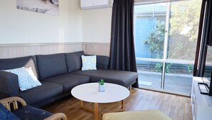 En moderne stue med en grå hjørnesofa, et rundt hvidt sofabord og udsigt til en have gennem et stort vindue.