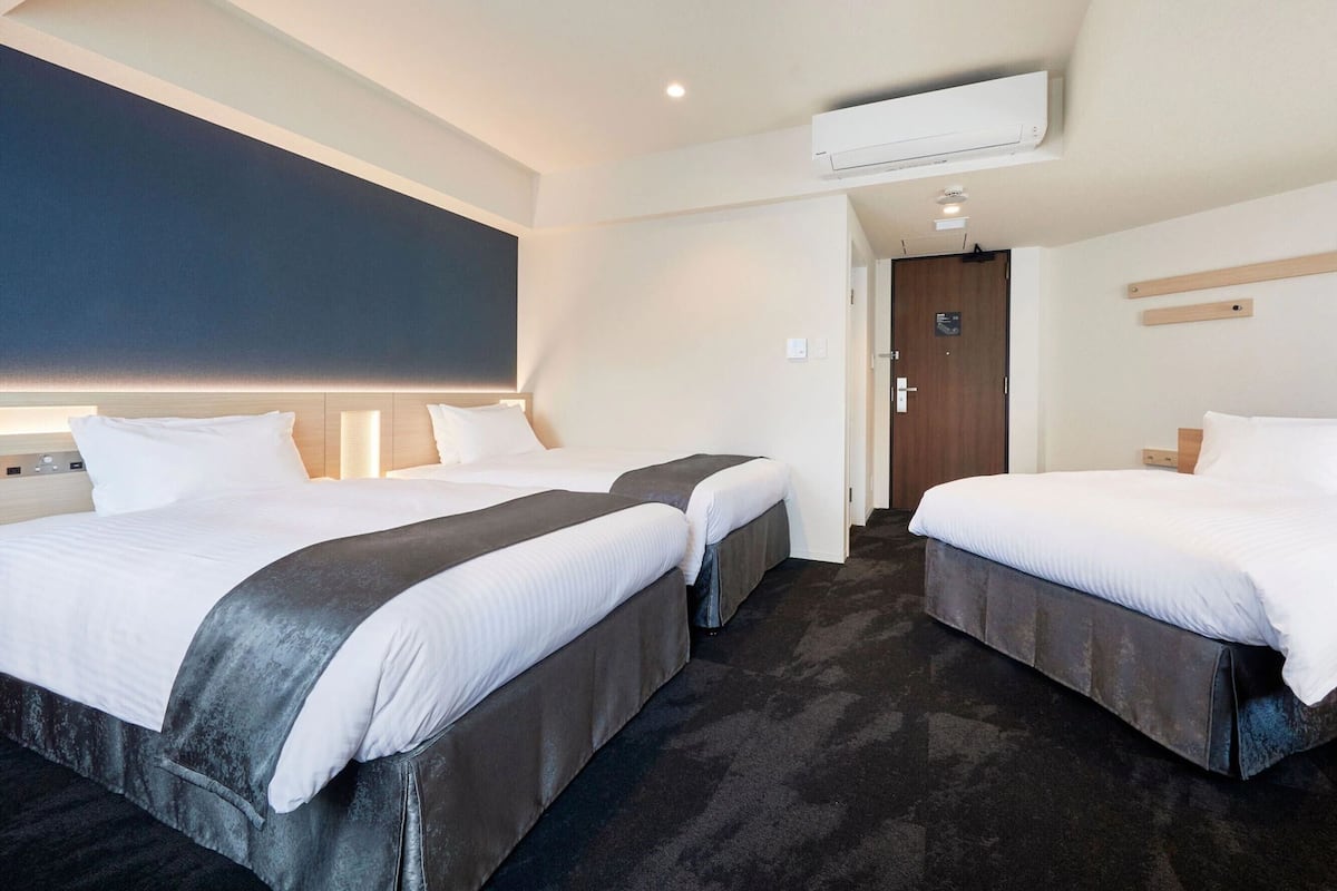 A hotel room with two beds, a dark carpet, a large window, and an air conditioning unit.