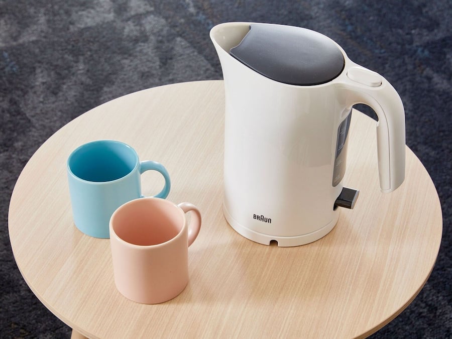 Ein weißes elektrisches Wasserkocher mit Henkel und Ausguss, zwei Tassen und ein Holztisch.
