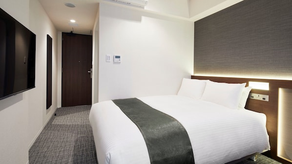A hotel room with a large bed, a flat-screen TV mounted on the wall, a door, and a wall-mounted light fixture. - Hotel Keyaki Gate Tokyo Fuchu (Fuchu)