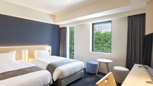 A hotel room with two beds, a desk, a chair, and a small table.