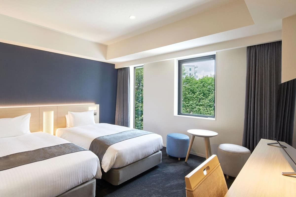 A hotel room with two beds, a desk, a chair, and a small table.