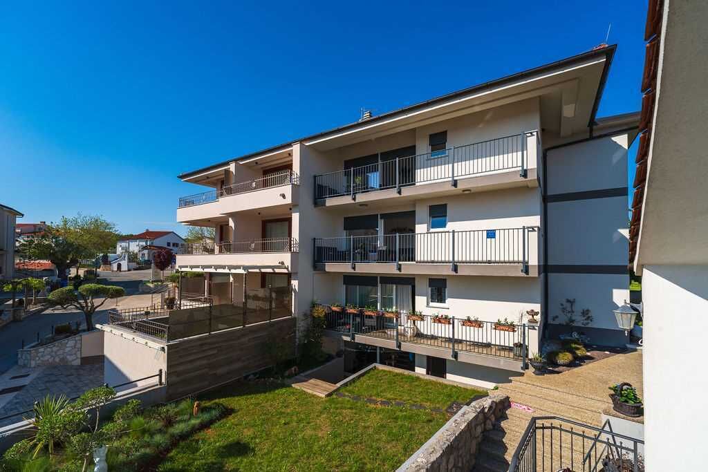 Un edificio residencial de varios pisos con balcones, un patio interior y un cielo azul despejado.