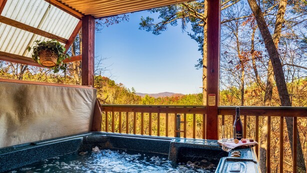 Un jacuzzi con terraza de madera y vista a árboles y montañas.