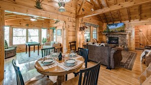 Interior de una cabaña de madera con comedor, sala de estar y chimenea.
