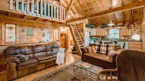 Una cabaña espaciosa de madera con un dormitorio en el altillo, una sala de estar acogedora con sofás de cuero y una cocina con gabinetes de madera.