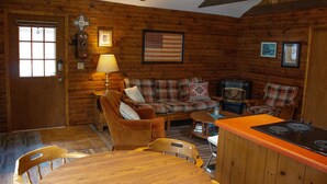 Ein gemütliches Blockhaus-Interieur mit Holzvertäfelung, einer Sofagarnitur, einem Esstisch und einem Holzofen.