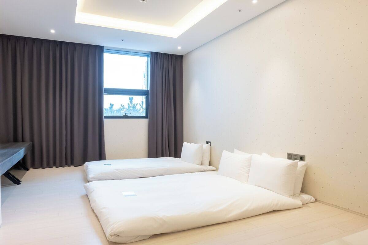A modern hotel room with two single beds, a desk, and a large window with curtains.
