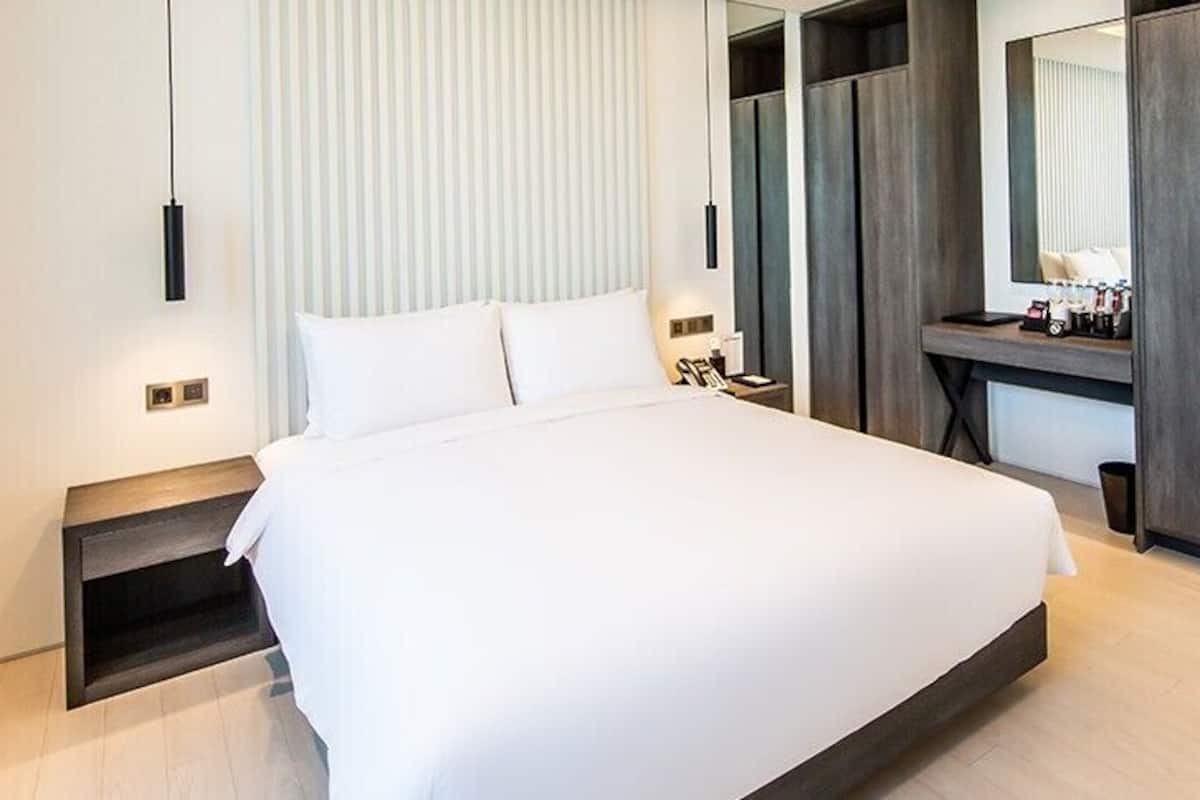 A modern hotel room with a large bed, a desk, and a wardrobe.