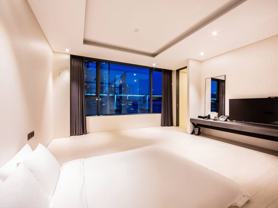 A modern hotel room with a large bed, a TV, and a city view.