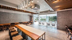 A modern restaurant with a long wooden table, multiple seating areas, and large windows offering views of the outdoors. - AG405 Hotel (Busan)