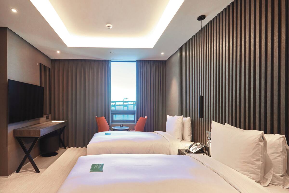 A hotel room with two beds, a TV, a desk, a phone, and a view of the city.