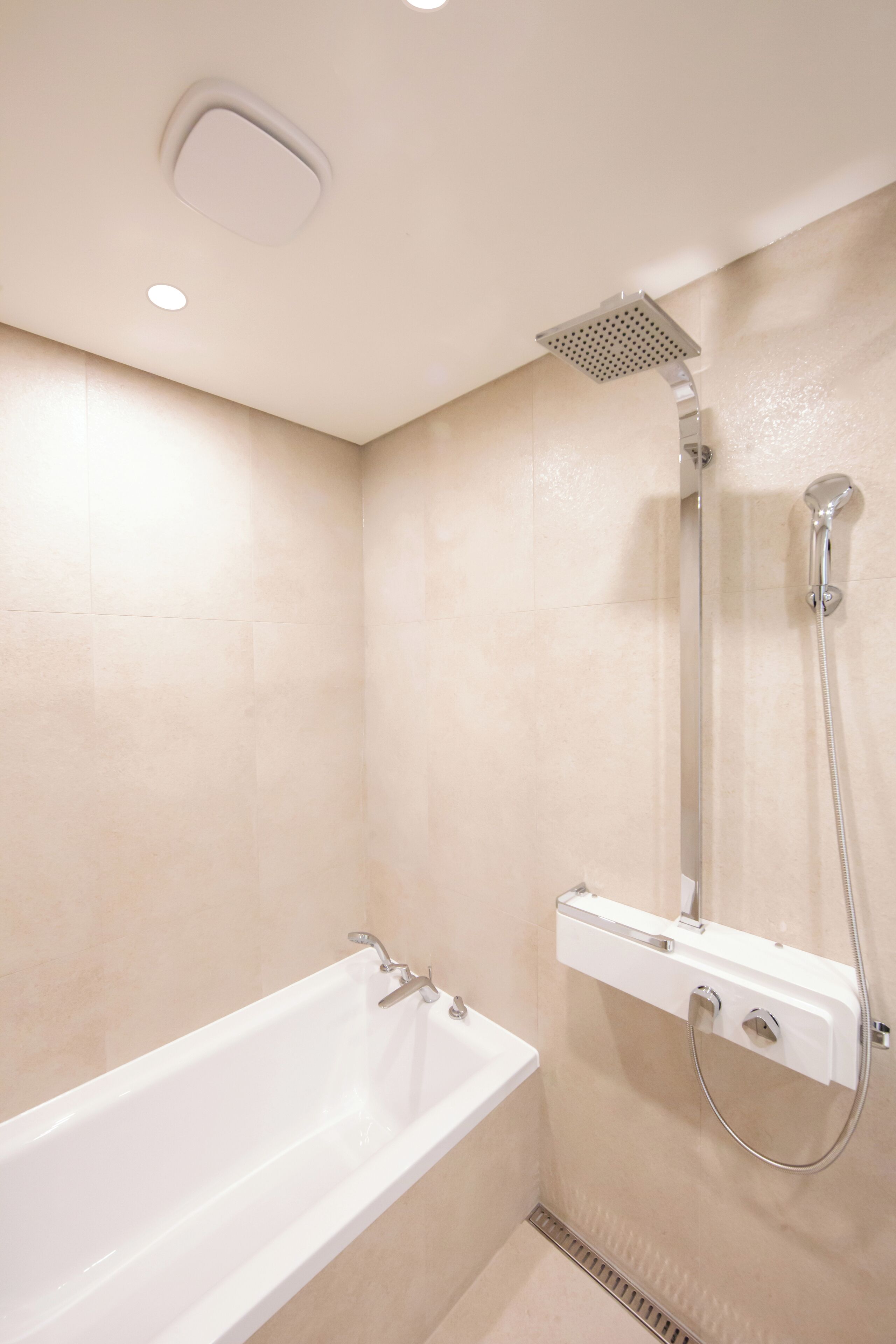 A modern bathroom with a bathtub, a shower with a handheld showerhead, and a wall-mounted control panel.