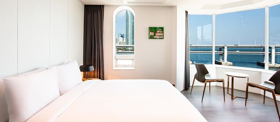 Habitación de hotel con una cama grande, un ventanal con vistas a la ciudad y un balcón con sillas.