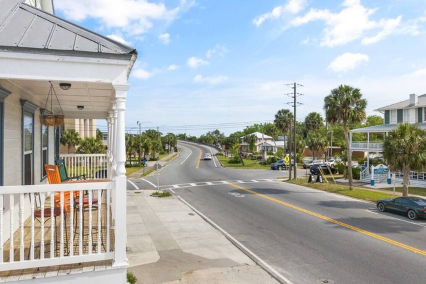 A street view with a white building featuring a porch with chairs and a railing.