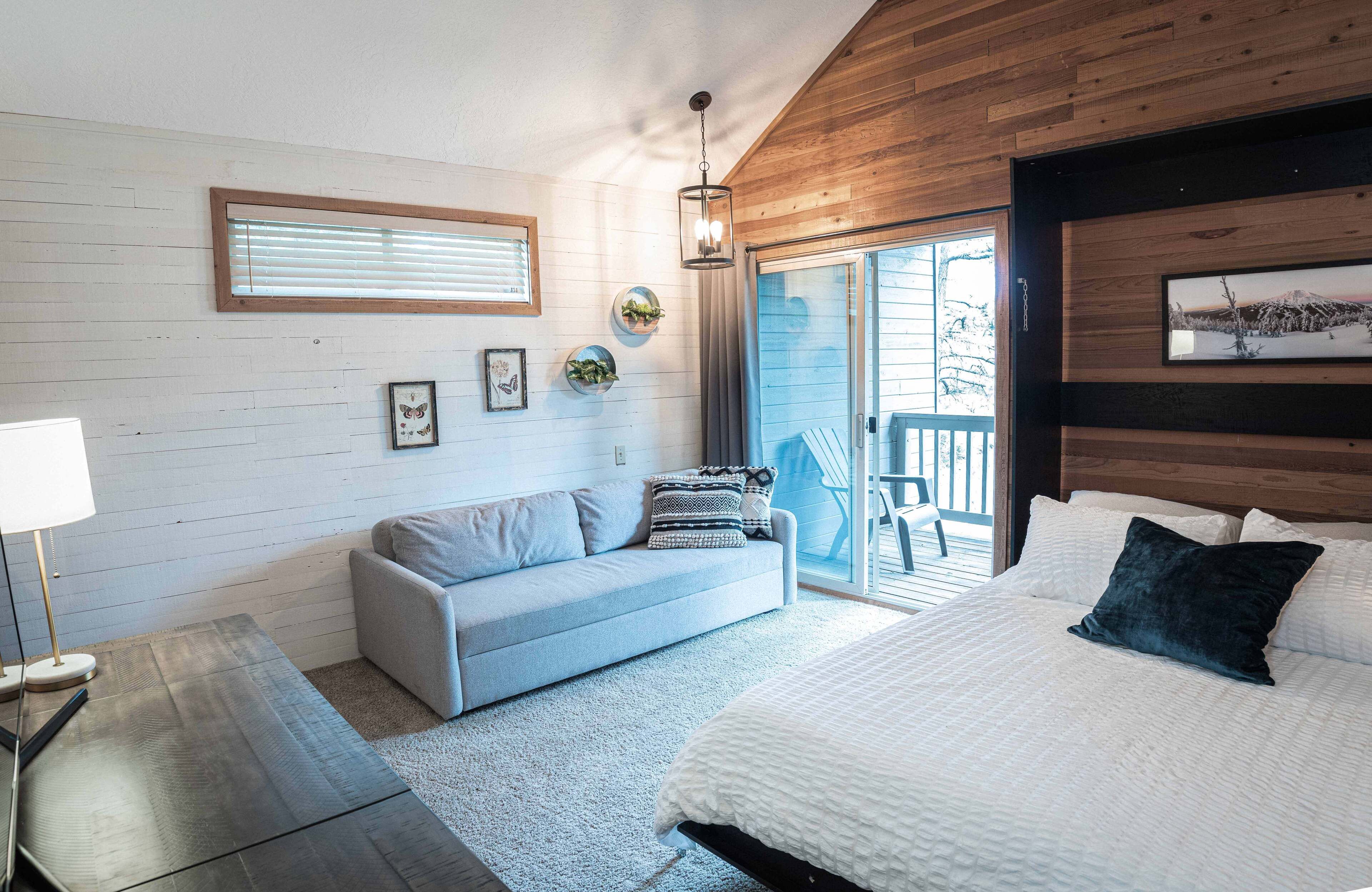 Une chambre à coucher avec un lit, un canapé, une lampe et une vue sur l’extérieur.