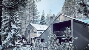 A two-story cabin with a balcony, surrounded by snow-covered trees. - Peaceful modern oasis -walking distance to Village (Sunriver)