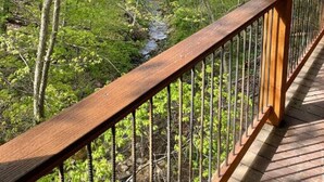 A wooden deck with a metal railing overlooking a forested area with a stream. - Dream Treehouse Getaway with Hot Tub (Millersburg)