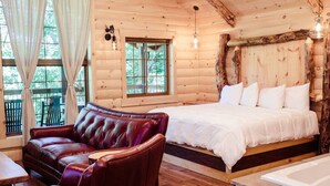 A log cabin room with a bed, a leather sofa, and a stone bathtub. - Dream Treehouse Getaway with Hot Tub (Millersburg)