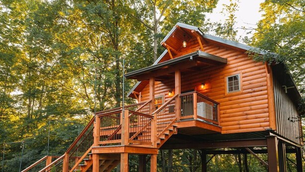 Een houten hut met een balkon en een trap, omringd door bomen.