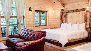 Een houten blokhutkamer met een bed, een leren bank en een ligbad van steen.