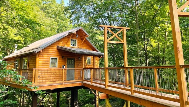 A wooden cabin with a deck, surrounded by dense forest. - Charming Treehouse Getaway with Treetop Views (Millersburg)