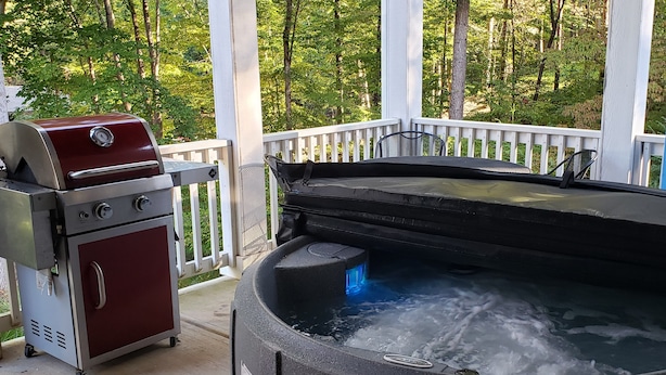 Un jacuzzi con una parrilla en un porche con barandilla blanca y árboles al fondo.