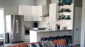 Una cocina moderna con armarios blancos, un refrigerador de acero inoxidable y una zona de bar con taburetes.