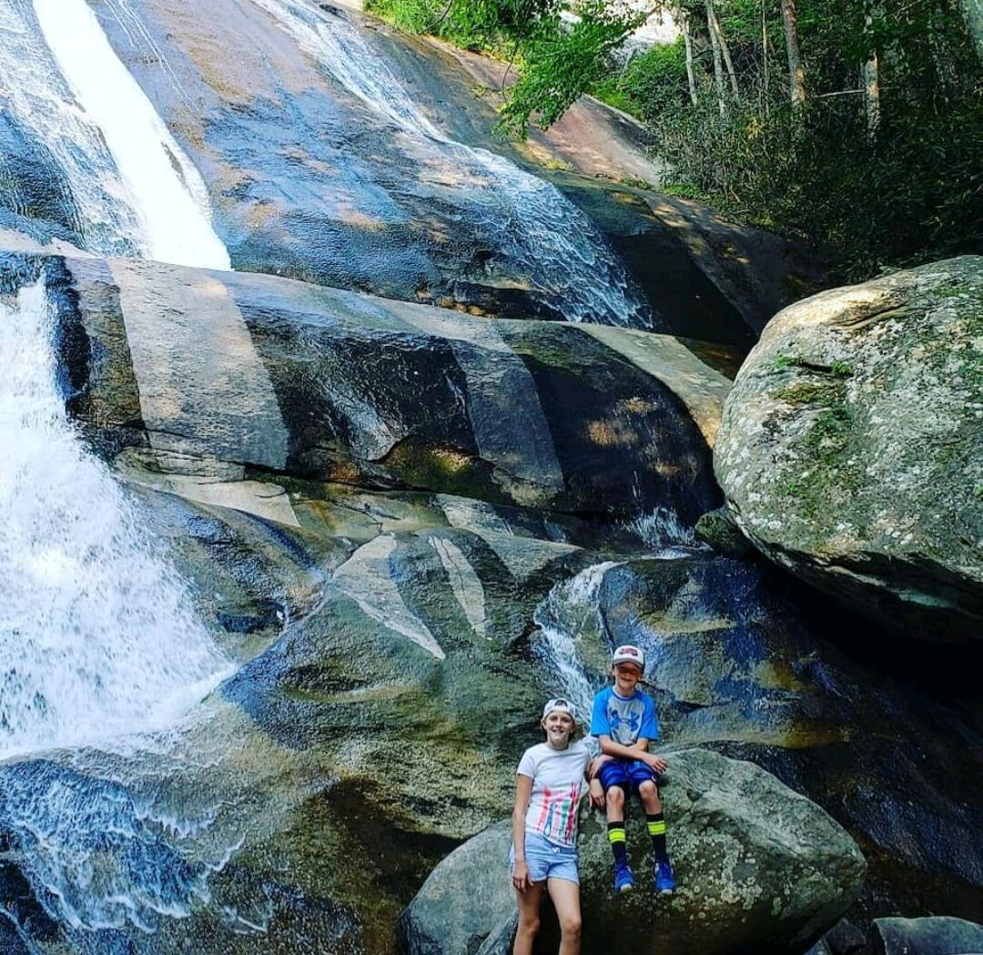 Une cascade d’eau se déversant sur de gros rochers, avec deux personnes assises sur un rocher au premier plan.