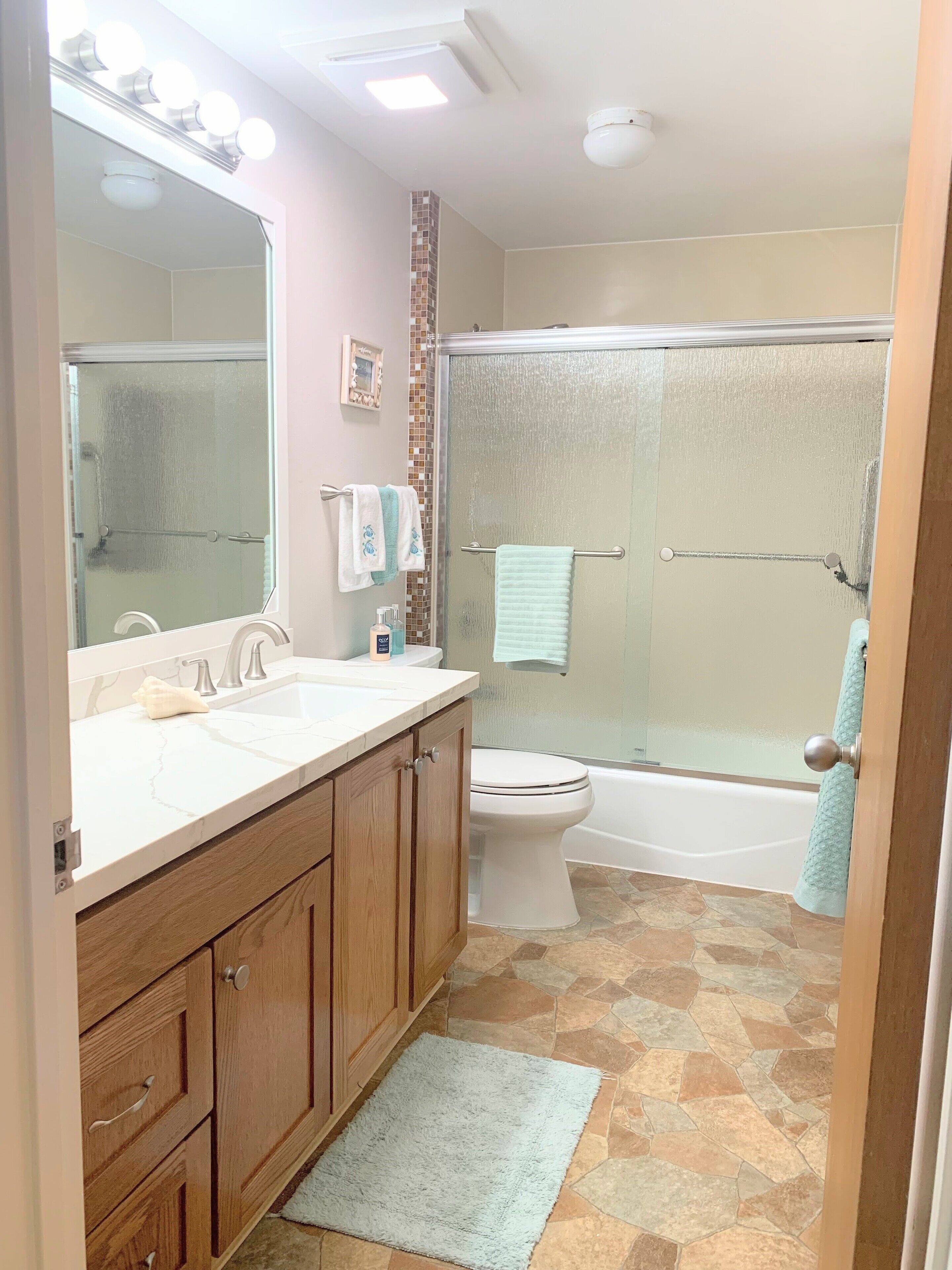 A bathroom with a large mirror, two sinks, a toilet, and a shower.