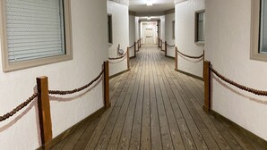 Un pasillo con piso de madera, paredes blancas y ventanas con barrotes.